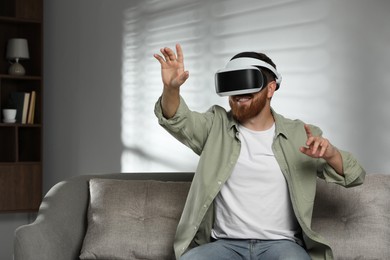 Photo of Smiling man using virtual reality headset on sofa at home. Space for text