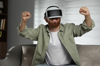 Photo of Happy man using virtual reality headset on sofa at home