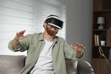 Photo of Smiling man using virtual reality headset on sofa at home