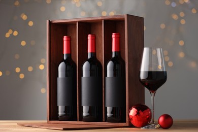 Wooden gift box with bottles of wine, glasses and red Christmas balls on table