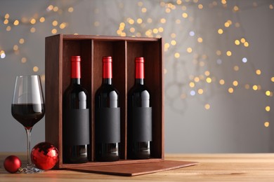 Wooden gift box with bottles of wine, glasses and red Christmas balls on table, space for text