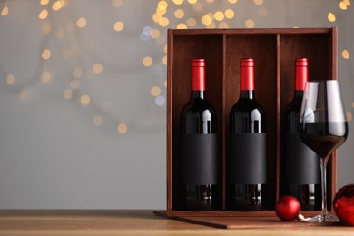 Wooden gift box with bottles of wine, glasses and red Christmas balls on table, space for text