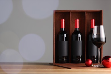 Wooden gift box with bottles of wine, glasses and red Christmas balls on table, space for text