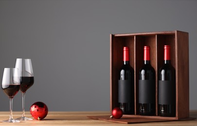 Wooden gift box with bottles of wine, glasses and red Christmas balls on table, space for text