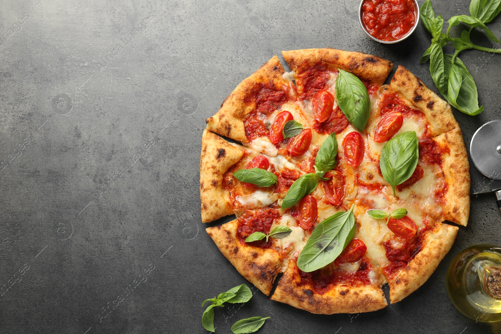 Photo of Delicious Margherita pizza, ingredients and cutter on grey table, top view. Space for text