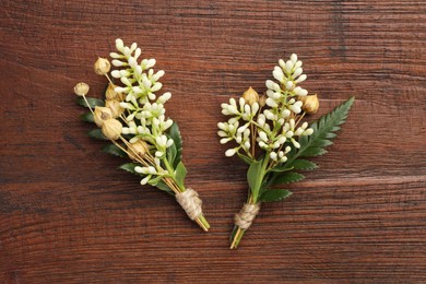 Photo of Small stylish boutonnieres on wooden table, top view