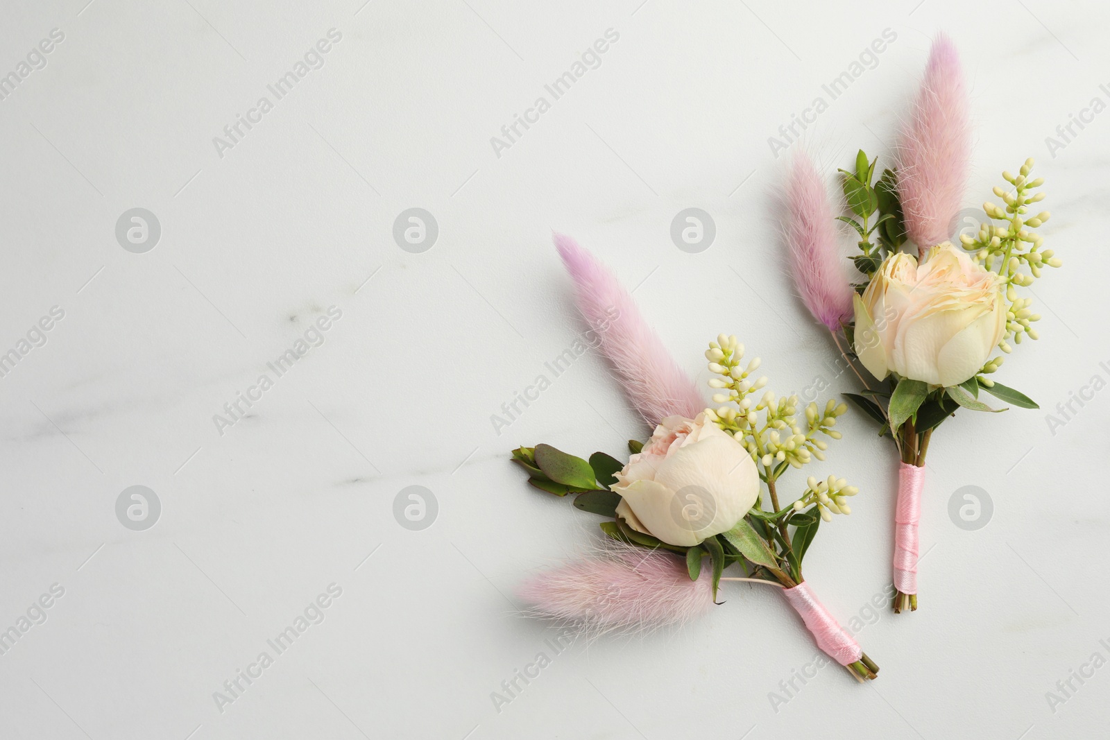 Photo of Small stylish boutonnieres on white marble table, top view. Space for text