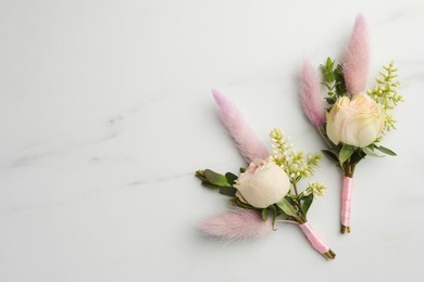 Small stylish boutonnieres on white marble table, top view. Space for text