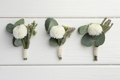 Photo of Small stylish boutonnieres on white wooden table, flat lay