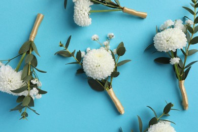 Many stylish boutonnieres on light blue background, flat lay