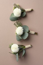 Small stylish boutonnieres on beige background, flat lay