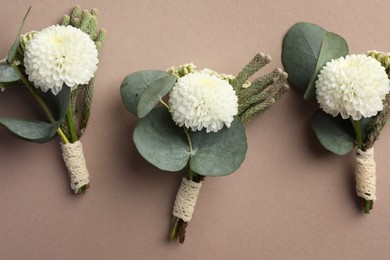 Photo of Small stylish boutonnieres on beige background, flat lay