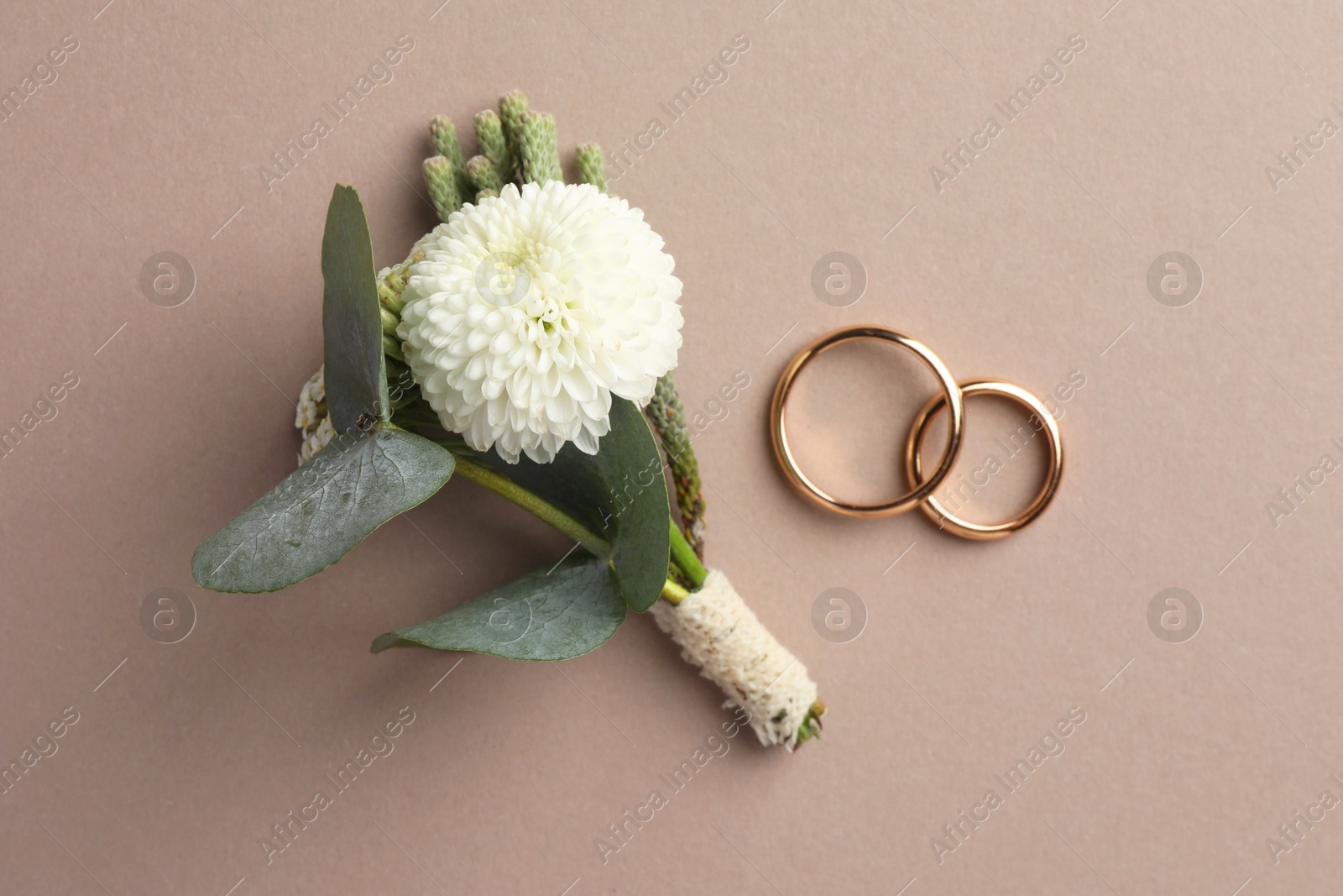 Photo of Small stylish boutonniere and rings on beige background, top view