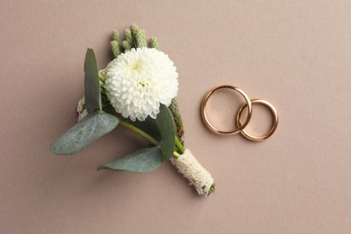 Photo of Small stylish boutonniere and rings on beige background, top view