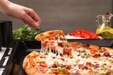 Photo of Woman taking piece of delicious pizza Diablo from baking tray, closeup