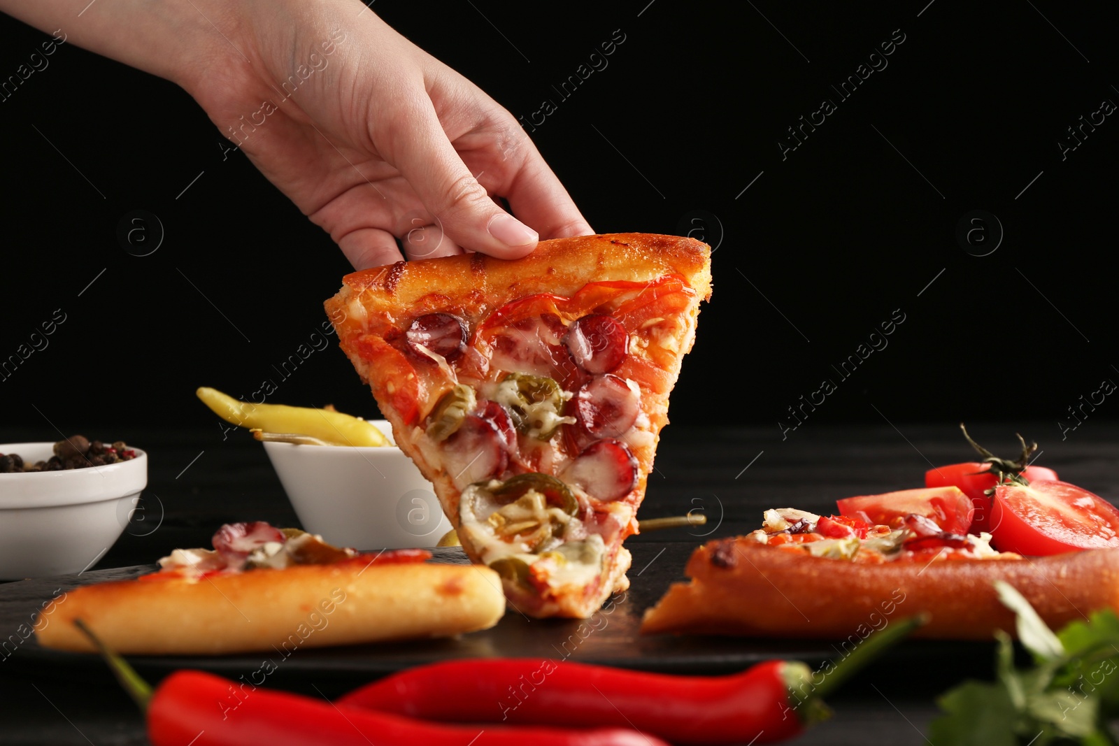 Photo of Woman taking piece of delicious pizza Diablo at table on black background, closeup