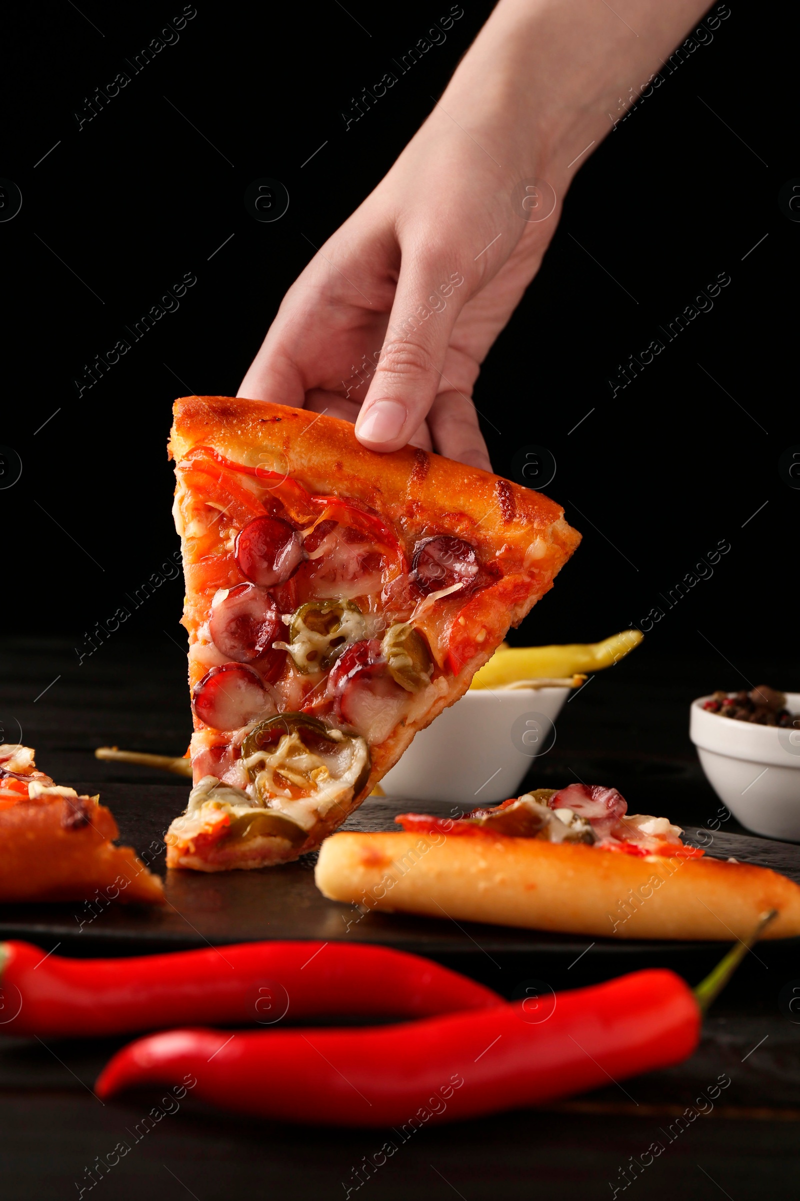 Photo of Woman taking piece of delicious pizza Diablo at table on black background, closeup