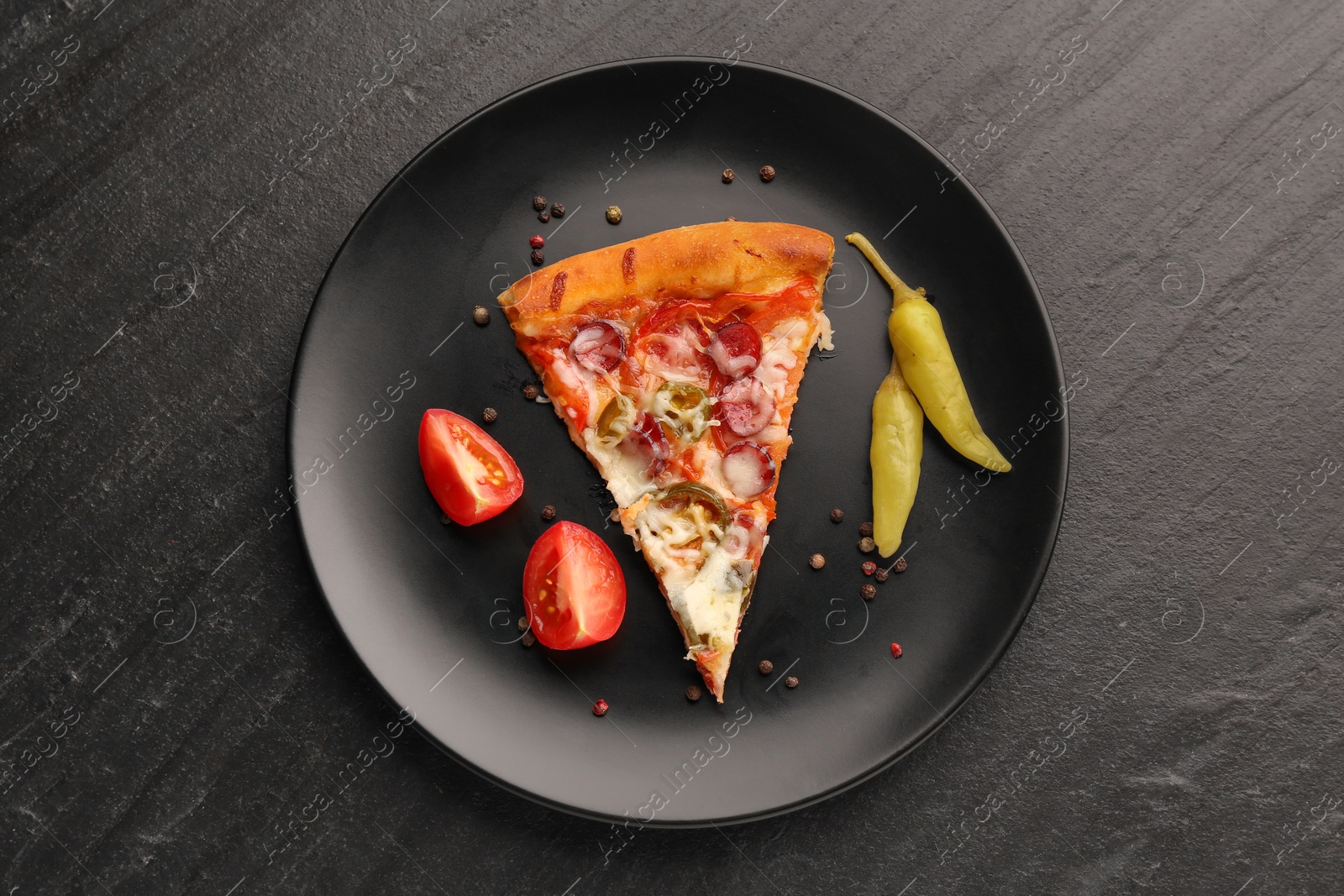 Photo of Plate with delicious pizza Diablo, pepper, tomato and peppercorns on dark textured table, top view