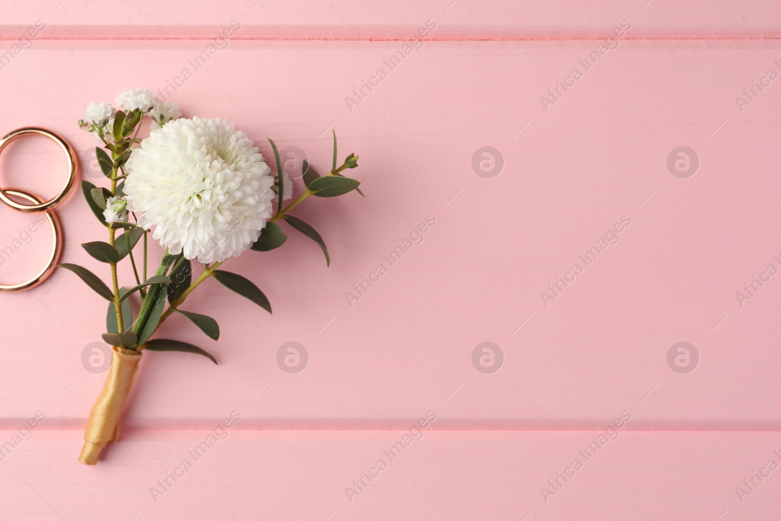 Photo of Small stylish boutonniere and rings on pink wooden table, flat lay. Space for text