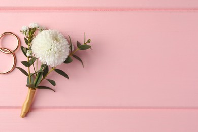 Small stylish boutonniere and rings on pink wooden table, flat lay. Space for text