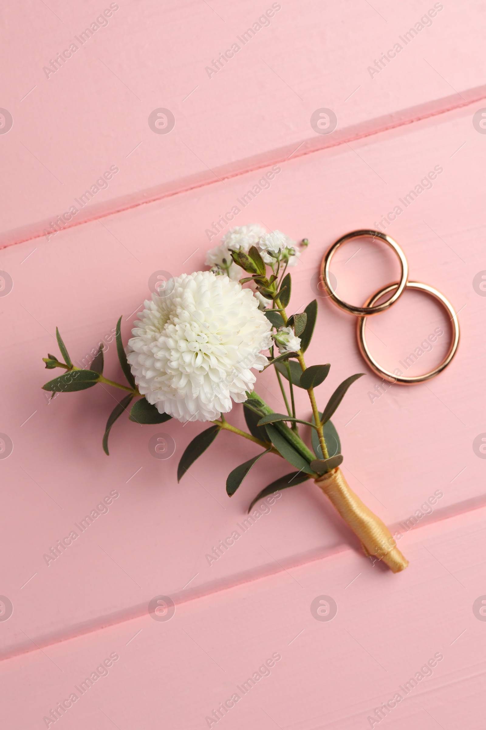 Photo of Small stylish boutonniere and rings on pink wooden table, flat lay