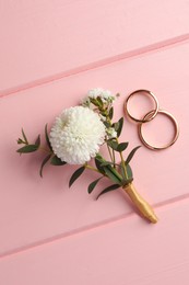 Photo of Small stylish boutonniere and rings on pink wooden table, flat lay