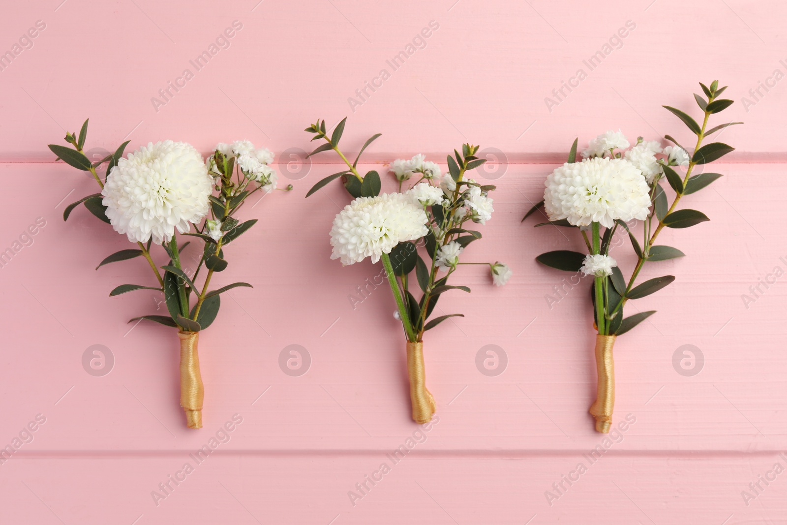 Photo of Many small stylish boutonnieres on pink wooden table, flat lay