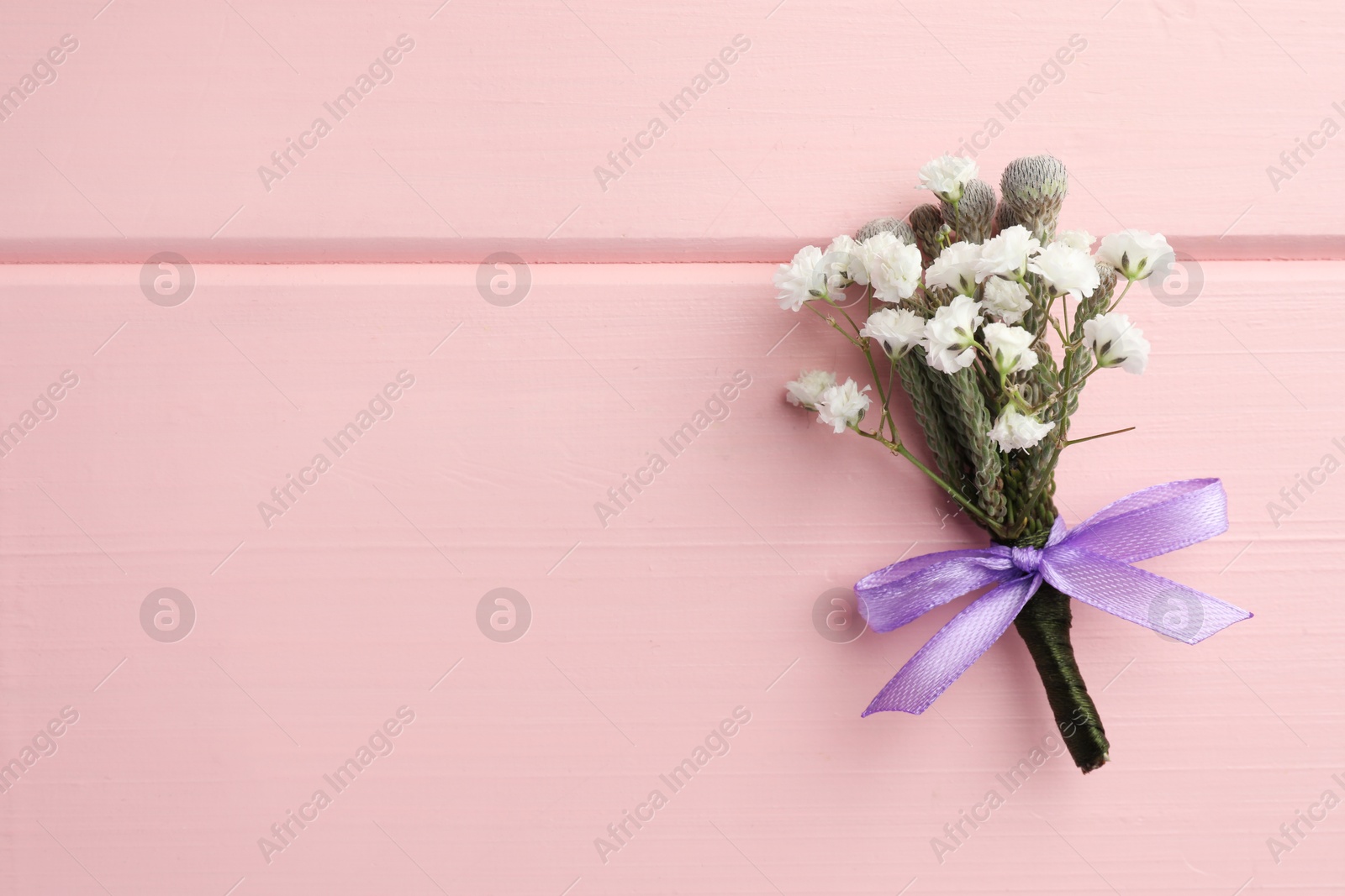 Photo of Small stylish boutonniere on pink wooden table, top view. Space for text