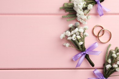 Small stylish boutonnieres and rings on pink wooden table, flat lay. Space for text