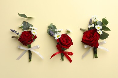 Many stylish red boutonnieres on beige background, flat lay