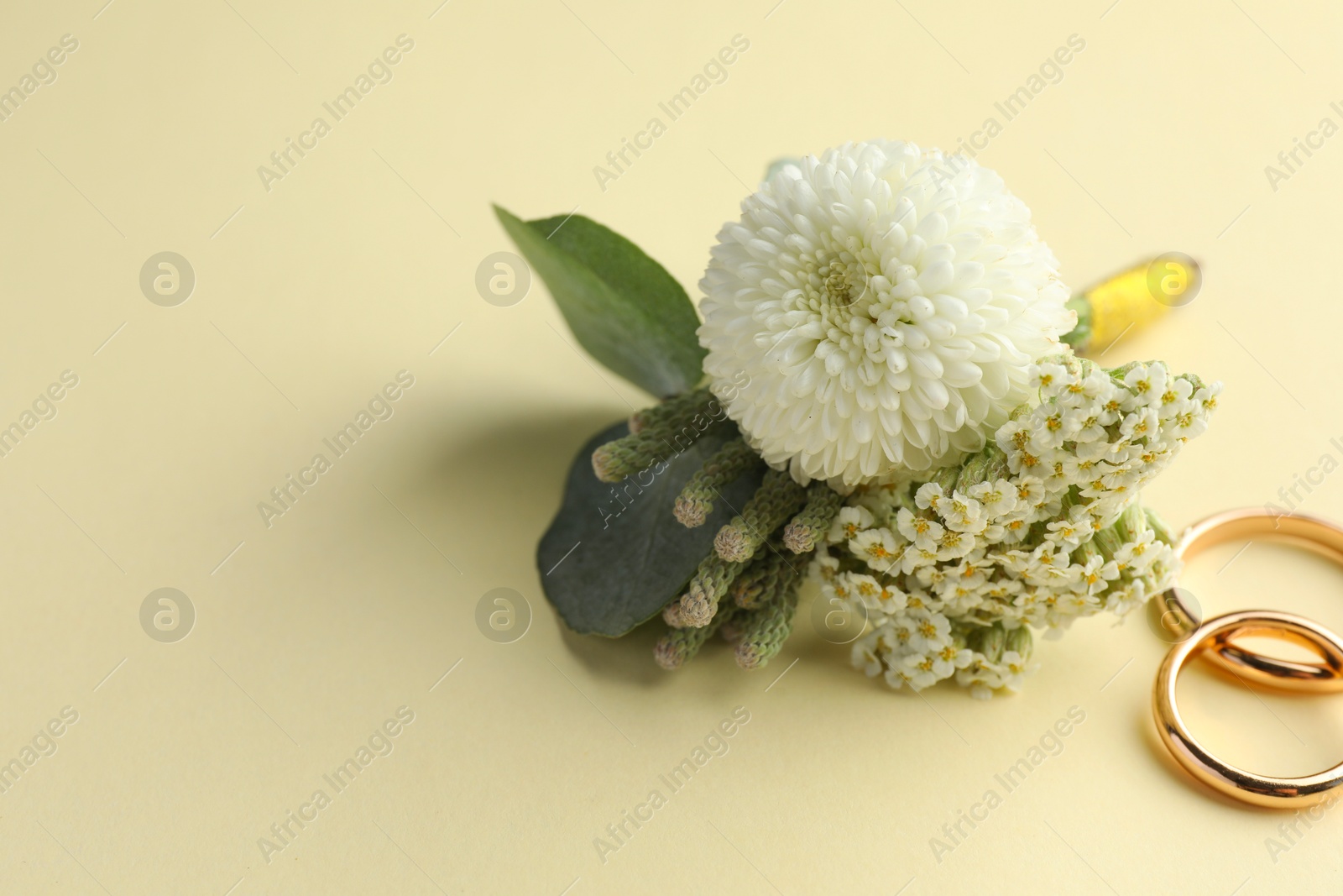 Photo of Small stylish boutonniere and rings on beige background. Space for text