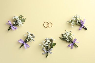 Small stylish boutonnieres and rings on beige background, flat lay