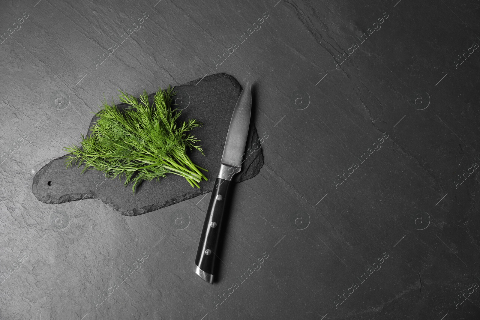 Photo of Sprigs of fresh green dill and knife on black table, top view. Space for text