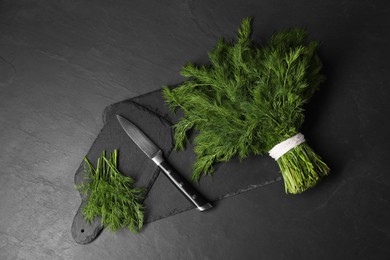 Photo of Sprigs of fresh green dill and knife on black table, top view