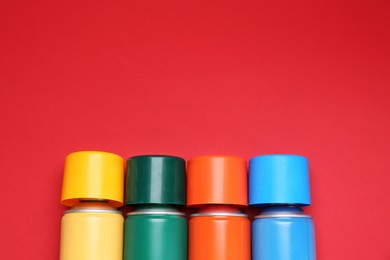 Photo of Many spray paint cans on red background, top view. Space for text