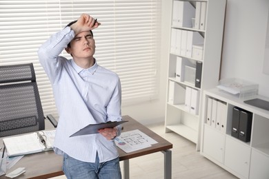 Photo of Embarrassed man with clipboard and pen in office