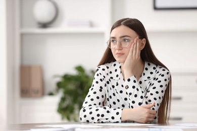 Photo of Embarrassed woman in glasses at table in office, space for text
