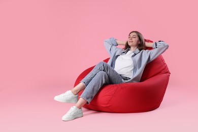 Photo of Beautiful young woman sitting on red bean bag chair against pink background, space for text