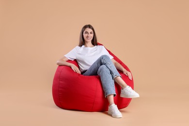 Photo of Smiling woman on red bean bag chair against beige background