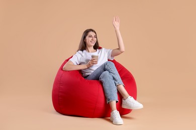 Photo of Smiling woman with paper cup of drink on bean bag chair against beige background