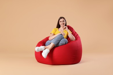 Photo of Smiling woman sitting on red bean bag chair against beige background