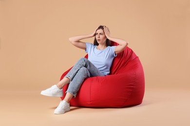 Photo of Emotional woman sitting on red bean bag chair against beige background