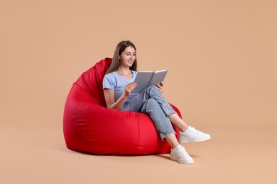 Photo of Smiling woman reading book on red bean bag chair against beige background