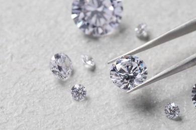 Photo of Tweezers with beautiful shiny diamonds on light textured background, closeup