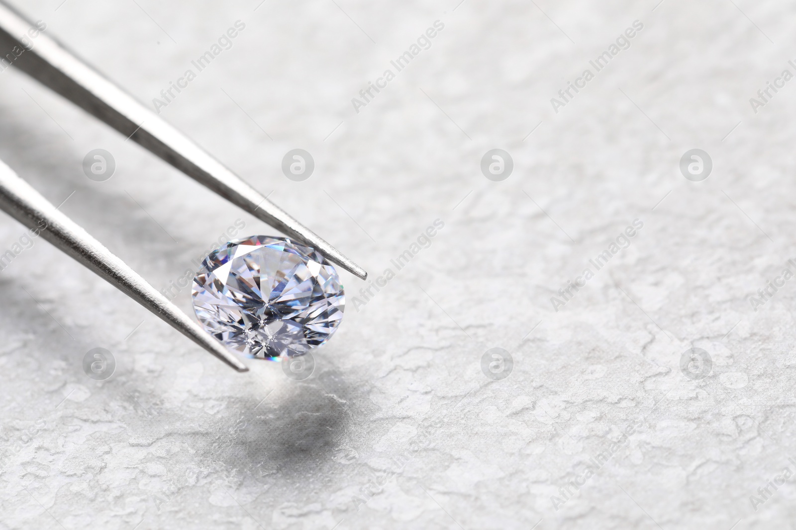 Photo of Tweezers with beautiful shiny diamond on light textured background, closeup. Space for text