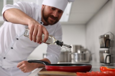 Photo of Professional chef pouring oil into frying pan in kitchen, selective focus