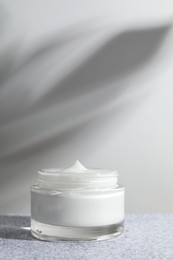 Photo of Face cream in jar on grey textured table. Cosmetic product