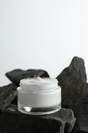 Photo of Face cream in jar on stones against light background