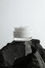 Face cream in jar on stones against light background