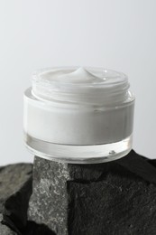 Face cream in jar on stones against light background, closeup